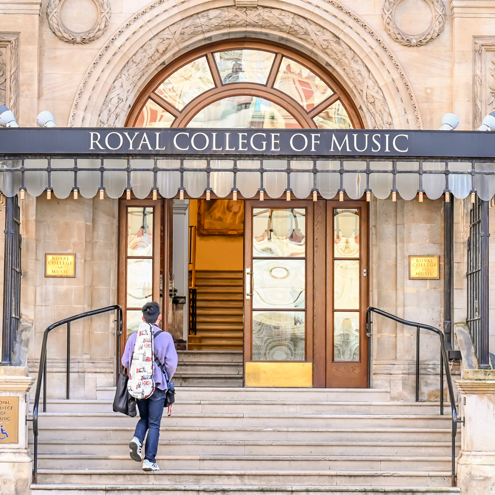 A student with a instrument case walking up the steps towards an open door, with the Royal College of Music sign above it